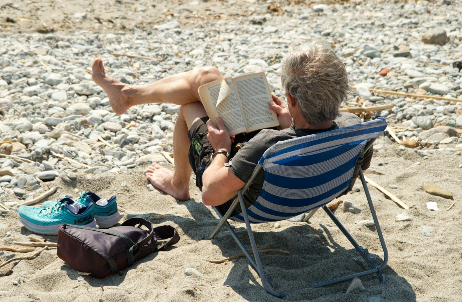 Person relaxing and reading a book on the beach.